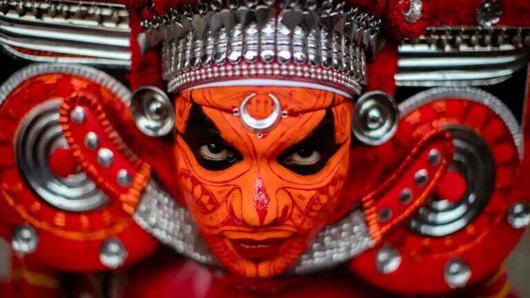 A Theyyam performer in vivid face paint and towering headdress, North Kerala